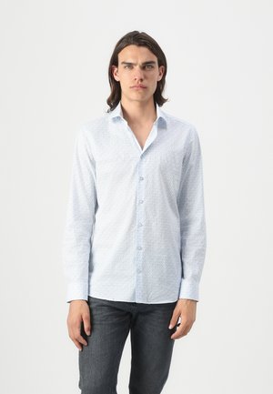 Light blue button-up shirt with small geometric patterns, made of cotton. Features a classic collar and long sleeves. Worn with dark jeans.