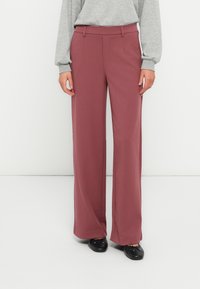 Wide-leg trousers in a soft, burgundy fabric. Features a smooth texture, tailored fit, and side pockets. Paired with black footwear.