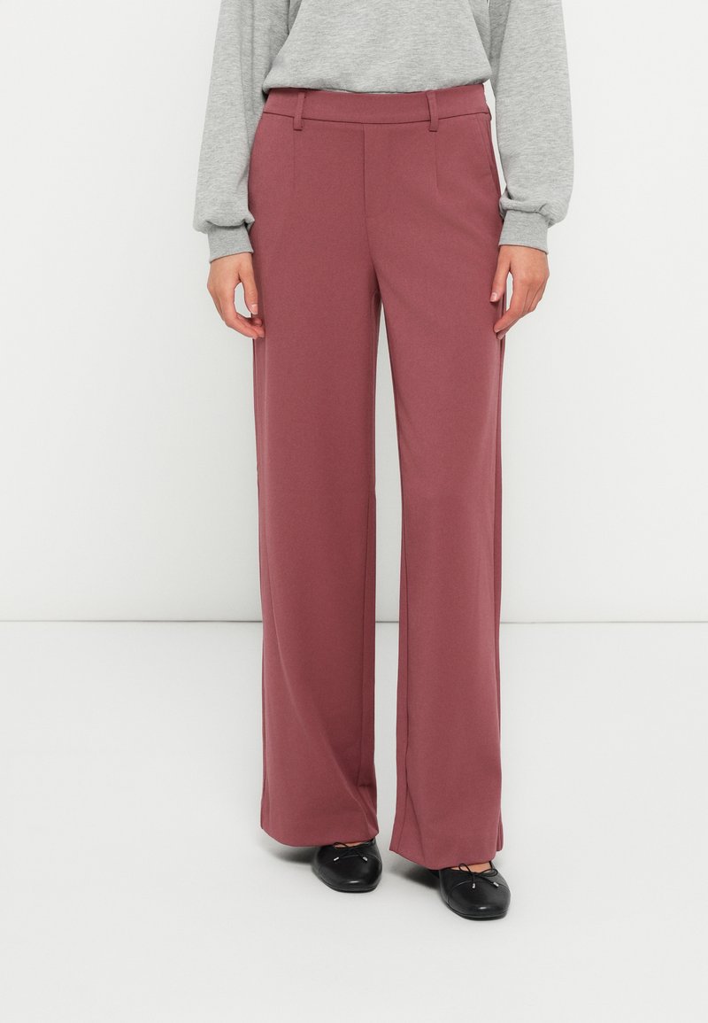 Wide-leg trousers in a soft, burgundy fabric. Features a smooth texture, tailored fit, and side pockets. Paired with black footwear.