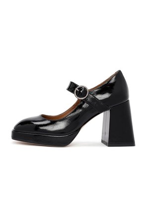 Black patent leather Mary Jane heels with a rounded toe, a circular buckle strap, and a chunky square heel. Textured detail on the sole.