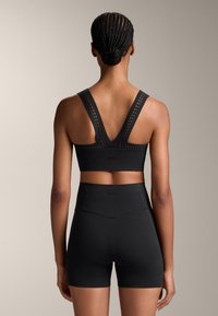 Black athletic bra with wide, perforated straps, and matching high-waisted shorts. Smooth texture; minimalist design. Back view.