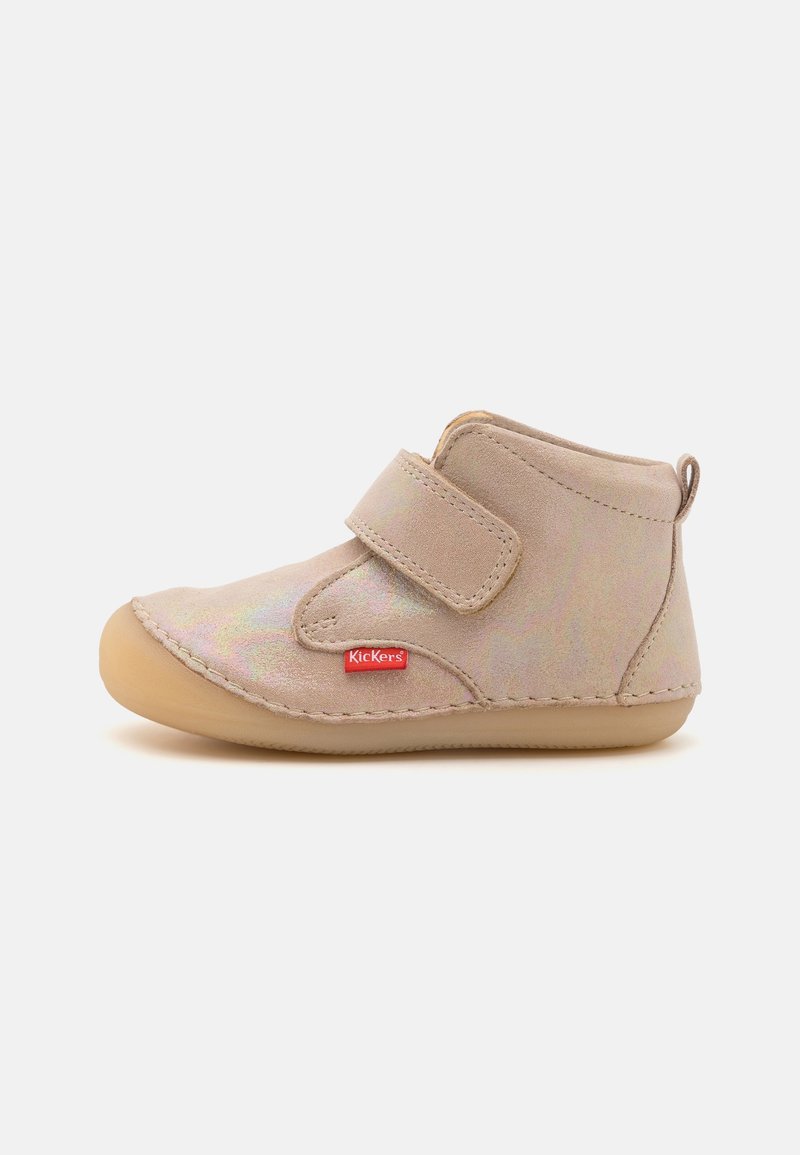 Chaussure beige en daim pour tout-petit avec bride Velcro réglable, semelle en caoutchouc arrondie et étiquette rouge avec le logo Kickers sur le côté.