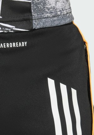 Shorts deportivos negros con un tejido liso y elástico. Los detalles notables incluyen rayas verticales blancas y un acento de cremallera naranja.