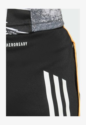 Pantaloni sportivi neri in tessuto morbido e elasticizzato. Dettagli notevoli includono strisce verticali bianche e una zip arancione.