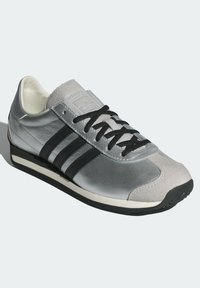 Srebrny skórzany sneaker z czarnymi paskami. Posiada zaokrąglony nosek, czarne sznurowadła oraz białą gumową podeszwę z minimalnym bieżnikiem.