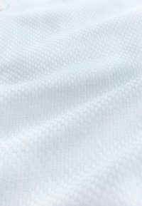 Zbliżenie na białą tkaninę o fakturze z delikatnym wzorem plastra miodu i miękkich fałd.