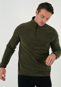 Mørkegrøn fleecepullover med halv-lynlås og lange ærmer. Blød tekstur, minimalistisk design og sort lynlåsdetalje.