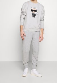 Sudadera gris con un estampado gráfico, cuello redondo y puños acanalados, combinada con pantalones de chándal grises a juego y zapatillas blancas.