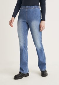 Ljusblå denimjeans med avslappnad passform och elastisk midja, med sidsömmar och subtila blekningar. Bärs med svarta platåboots.