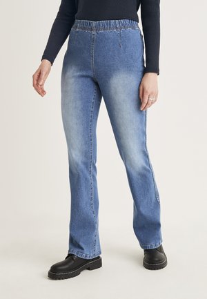 Jeans en denim bleu clair avec une coupe décontractée et une taille élastique, featuring des coutures latérales et une légère décoloration. Portés avec des bottes à plateforme noires.