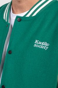 Zelená vyšívaná varsity bunda so pruhovaným golierom, čiernymi cvočkami a bielym nápisom "Kaotiko society".
