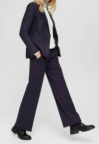 Laivastonsiniset raitakuvioidut bleiseri yhdistettynä leveälahkeisiin tummanvioletteihin housuihin. Alla teksturoitu valkoinen neule, jota täydentävät mustat nilkkurit.