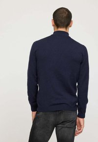 Pull à col rond bleu marine en tissu tricoté, doté de manches longues et d'une silhouette ajustée. Texture douce avec des poignets et un ourlet côtelés.