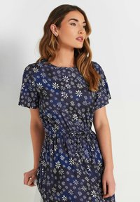 Marinblå klänning med vita blommönster, korta ärmar, rund halsringning och resårmidja för en figursydd silhuett.