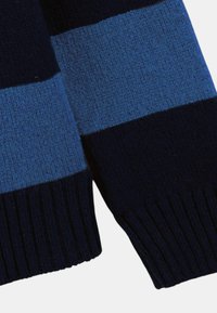 Écharpe en tricot à rayures horizontales bleues et noires avec des bords côtelés sur fond blanc.