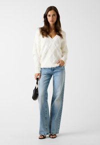 Maglione bianco e morbido con motivo a diamante, scollo a V e polsini a coste; abbinato a jeans a gamba larga azzurri chiaro e borsa nera.