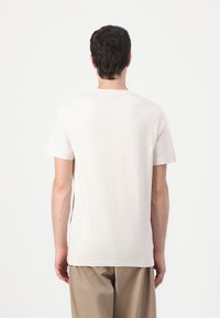 T-shirt beige clair en tissu doux et texturé, avec des manches courtes et un col ras du cou, associé à un pantalon marron clair.