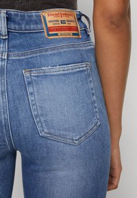 Jeans de mezclilla azul con bolsillos traseros, una etiqueta de cuero con "Diesel Industry" y detalles de costura visibles en la cinturilla.