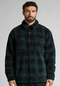 Chemise-jacket en polaire à carreaux noirs et teal, avec un col, une fermeture à boutons et deux poches avant, présentant une finition douce et texturée.