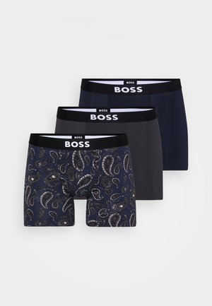 Drei Paare Herren-Boxershorts. Eine hat ein blaues Paisleymuster; die anderen sind einfarbig in Dunkelblau und Grau. Alle haben einen schwarzen Bund mit "BOSS"-Logo.