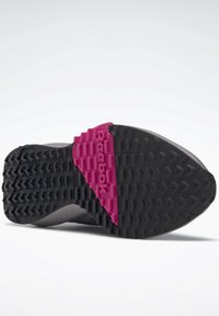 Semelle de chaussure avec motif de grip texturé noir et une partie rose au centre présentant le logo Reebok en lettres en relief.