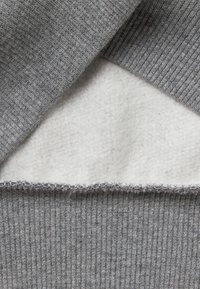 Grauer Strickpullover mit glatter weißer Fleecefutter. Verfügt über eine gerippte Textur und kontrastierende Nähte entlang des unteren Saums.