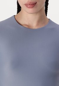 Ljust lila topp med en mjuk, elastisk textur och rund halsringning. Tyget verkar figurnära och framhäver silhuetten.