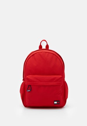 Mochila roja con bolsillo delantero con cremallera, bolsillos laterales, asa superior y pequeño parche con el logo de Tommy Hilfiger en el bolsillo frontal.