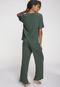 Zeleni rebrasti pleteni lounge set koji se sastoji od slobodno krojene majice s kratkim rukavima i hlača širokih nogavica, dizajniran za udobnost i lakoću pokreta.