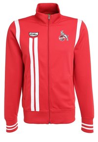 Veste de survêtement rouge zippée avec des bandes blanches, des poignets et un col côtelés. Présente un logo sur la poitrine gauche et une texture en tissu synthétique lisse.