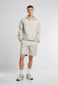 Lys grå zip-up jakke med elastiske mansjetter, kombinert med matchende shorts. Begge har en jevn tekstur og subtile sideakenter.