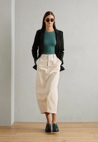 Černý blazer, těsně padnoucí tyrkysový top, dlouhá krémová sukně a tmavě zelené boty. Hladké textury, minimalistický design a neutrální barevná paleta.