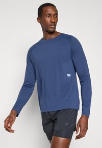 Navy long-sleeve athletic shirt made of smooth fabric, featuring a crew neck and a small logo on the left side, paired with black shorts.
