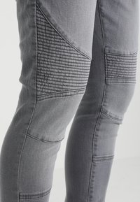 Jeans grises que presentan paneles de textura acanalada, corte ajustado y detalles de costura, fabricados en denim con una superficie suave.