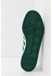 Green rubber sole of a shoe with a wavy texture, featuring a circular logo and "adidas" branding, showing a white upper with green accents.