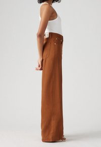 Ruske leve bukser lavet af denim, med høj talje, store lommer og sølvfarvede detaljer. Glat tekstur med minimal udsmykning.