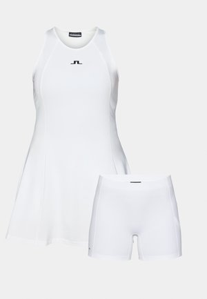 Vestido de tenis blanco sin mangas con falda acampanada, hecho de un tejido suave, combinado con pantalones cortos ajustados a juego. Acento de logo negro en el vestido.