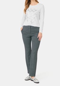 Camicia bianca a maniche lunghe con motivo a croce lucido, abbinata a pantaloni a pois bianchi e neri. Il modello indossa mocassini argento.