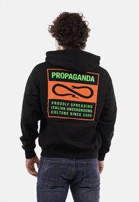 Felpa nera in cotone con una grafica arancione sul retro. Presenta testo verde, un elemento di design circolare e una tasca a marsupio.