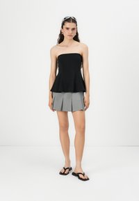 Top peplum nero senza spalline in tessuto lucido, abbinato a una mini gonna plissettata grigia e infradito nere. Design semplice e moderno.