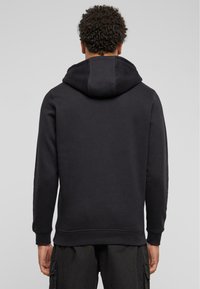 Felpa nera realizzata in misto cotone, con cappuccio regolabile, polsini e orlo a costine, che presenta un design semplice e minimalista.