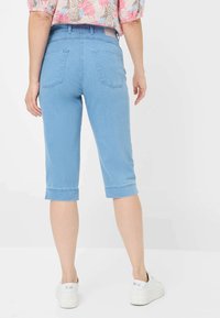 Pantaloni capri in denim blu chiaro con risvolti, cinque tasche e vita a media altezza, abbinati a scarpe da ginnastica bianche.