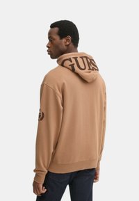 Felpa marrone con un grande logo sulla cappuccio, polsini e orlo a coste, con una texture sottile. Dettagli ricamati sui lati.