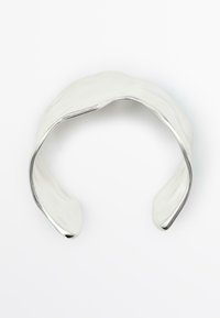 Silverfärgad metallarmband med en slät, polerad yta, mjuka kurvor och en öppen design. Har en lätt vågformad struktur.