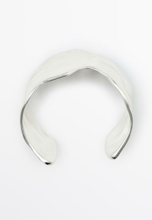 Bracciale in metallo argentato con superficie liscia e lucida, curve delicate e design aperto. Presenta una leggera texture ondulata.