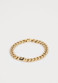 Bracelet en chaîne dorée avec des maillons épais et un emblème rectangulaire noir et or comportant un petit détail en forme de fleur, fermoir visible.