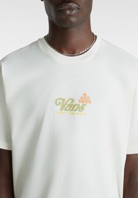 Camiseta de algodón blanca con un colorido logo de "Vans Off The Wall". El diseño incluye acentos en verde, naranja y amarillo en el pecho.