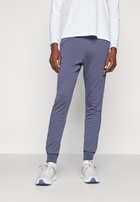 Grå träningsbyxor i en tapered design med ribbade muddar, tillverkade av ett mjukt material. Matchas med en lång vit skjorta och löparskor.