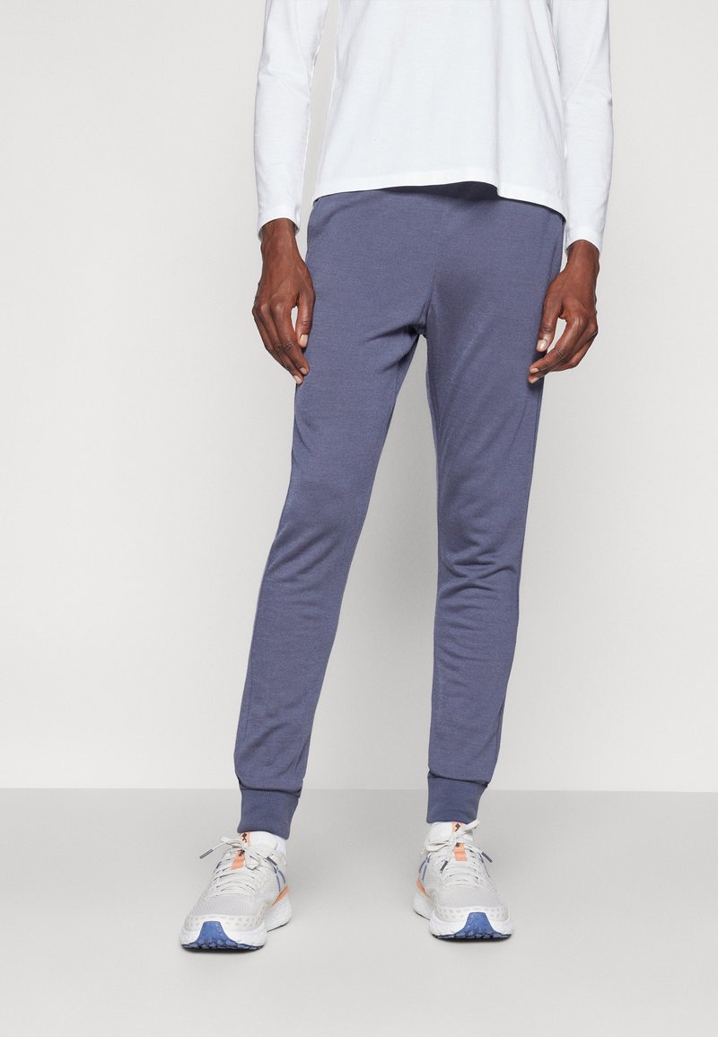 Grå träningsbyxor i en tapered design med ribbade muddar, tillverkade av ett mjukt material. Matchas med en lång vit skjorta och löparskor.