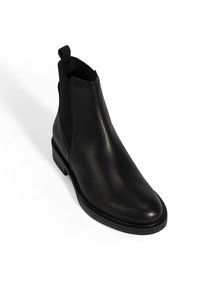 Bottine Chelsea en cuir noir avec panneaux latéraux élastiques, bout étroit, talon cranté et languette. Texture lisse, design minimaliste.